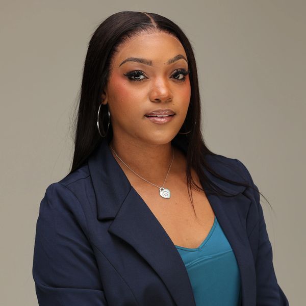 Confident woman in a navy blazer and teal top poses against a neutral background.