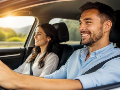 Happy couple driving a car together, enjoying a sunny day.
