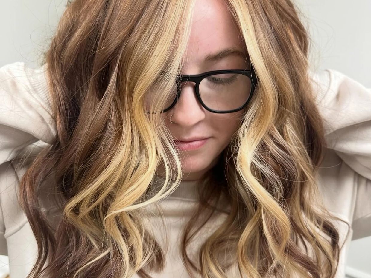 a girl wearing glass pulling her hair forward to show off the color and cut