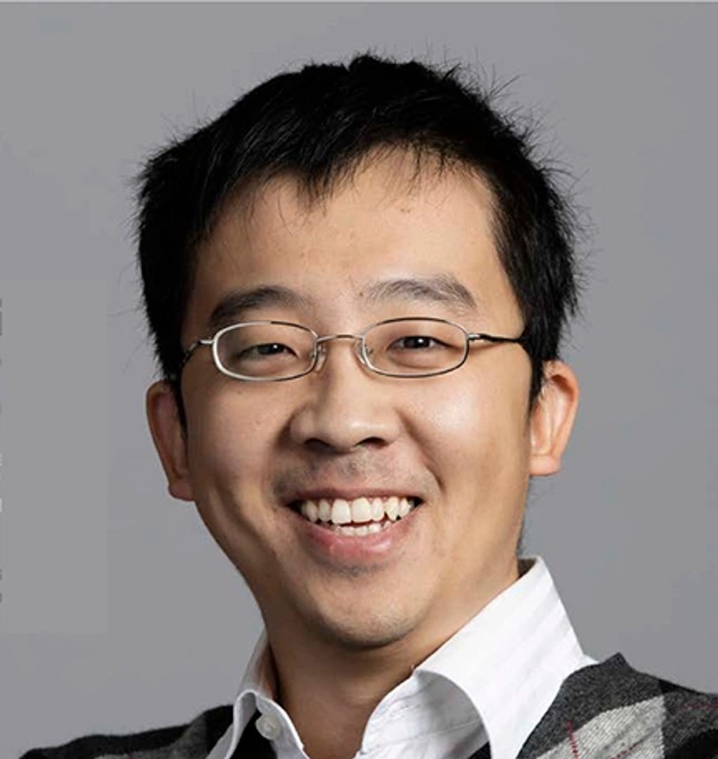 Smiling man wearing glasses and a checkered sweater.