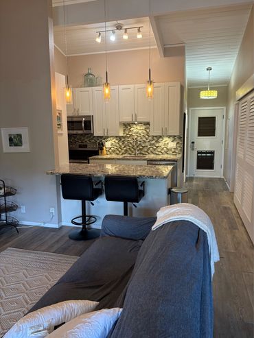 Open kitchen and hallway shown from coztyliving room, featuring warm lighting & granite countertops.