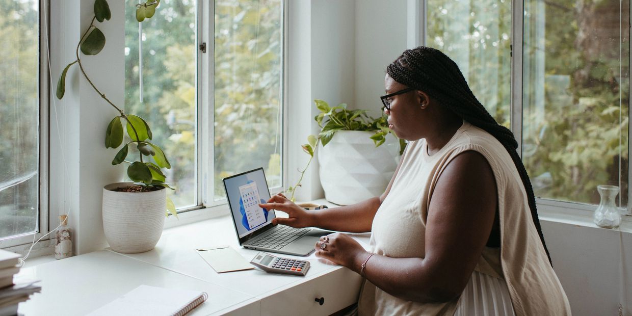 Woman on the computer working in surrounded two panes of windows with greenery around her
