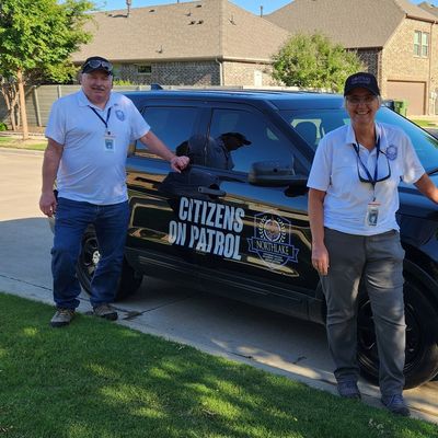 Two citizens on patrol standing beside a marked patrol vehicle in a neighborhood.