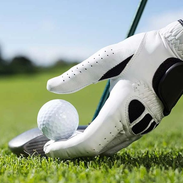 A gloved hand placing a golf ball on the grass with a club in the background.