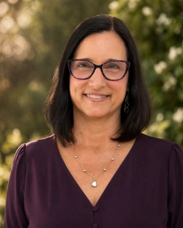 Woman with glasses smiling outdoors.