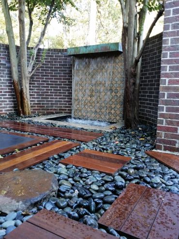 Outdoor water feature with wooden stepping stones and pebbles.