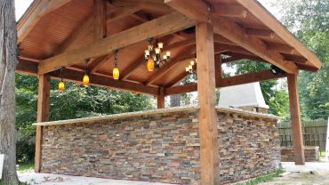 Outdoor wooden gazebo with stone bar counter and hanging lights.