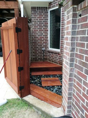 Wooden gate opening to a decorative patio area with black stones.