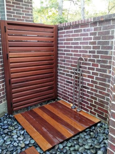 Outdoor wooden shower with pebble flooring.