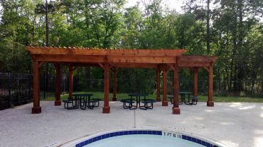 Wooden pergola with picnic tables near a pool.