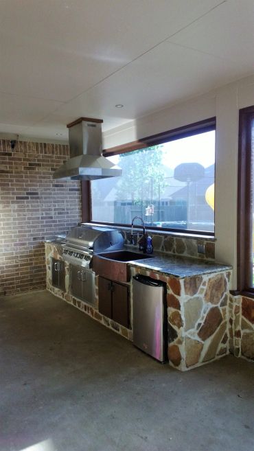 Outdoor kitchen with stone countertop and stainless steel appliances.