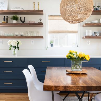 Modern kitchen with navy cabinets and wooden dining table with yellow flowers.