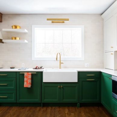 Modern kitchen with green cabinets, white countertops, and a gold faucet under a large window.