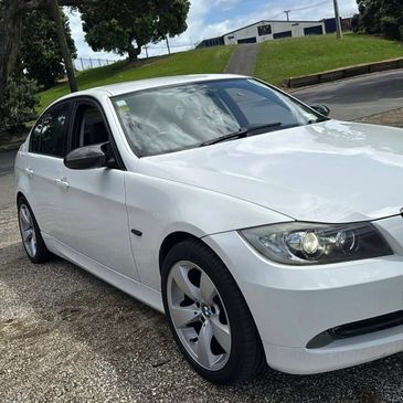 White BMW sedan parked on a gravel surface under a partly cloudy sky.
