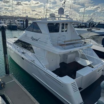 White yacht named Rascal docked at a marina under a cloudy sky.