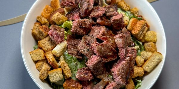 Steak salad with croutons in a white bowl.