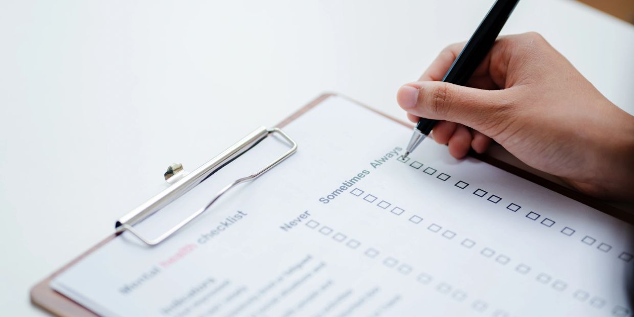 Person filling out a mental health checklist with a pen.