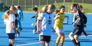 Girls playing soccer on a blue field.