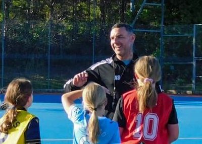 Coach talking to young girls in sports uniforms on a field.