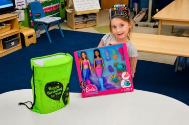 A young girl holding a Barbie mermaid doll set while celebrating her birthday.