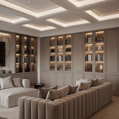 A modern living room with elegant beige sofas and built-in illuminated shelves.