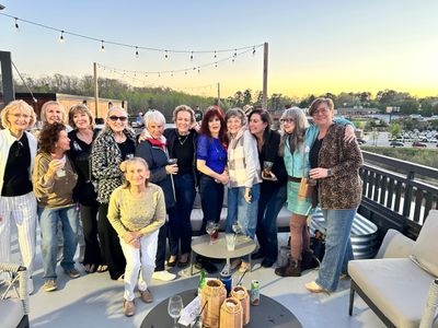 Group of women enjoying a sunny rooftop gathering with drinks and smiles.