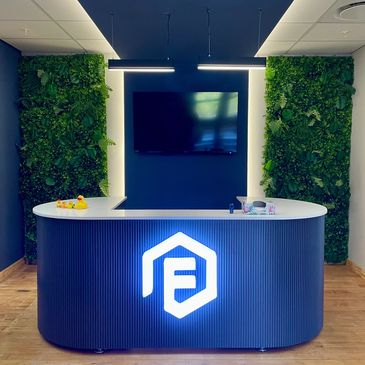 Modern reception desk with illuminated logo and greenery walls.