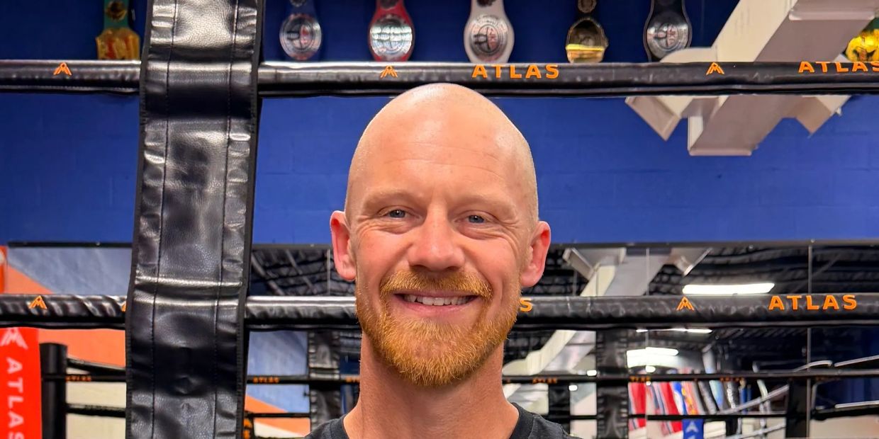 Smiling bald man with a ginger beard in a gym.