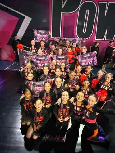 A large group of cheerleaders celebrating multiple 1st place wins with banners and trophies.