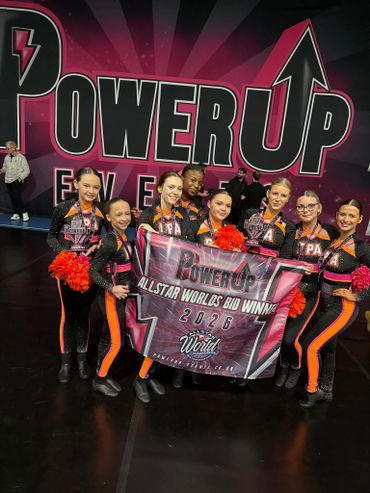 Cheerleading team celebrating their 2026 Allstar Worlds bid win with a banner and pom-poms.