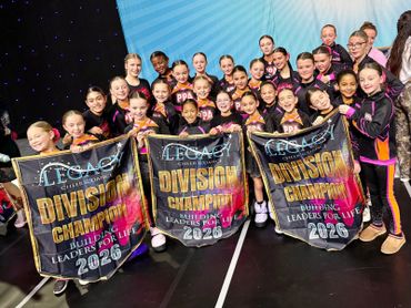 Youth dance team proudly holding three division champion banners from 2026.