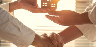2 people shaking hands and holding a house