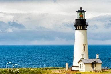 Yaquina Head Lighthouse stands tall under sunny skies as distant clouds approaches, in Newport, Oreg