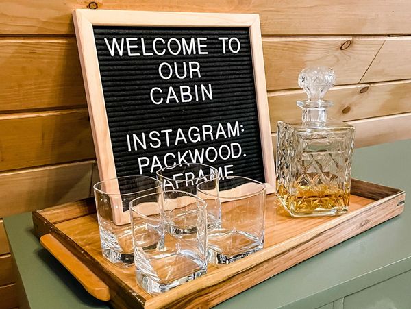 Decanter of whiskey next to four glasses, placed in front of a letter board that says "welcome to ou