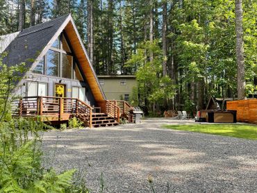 A-frame cabin in a forested area with gravel driveway.