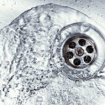 Close-up of water swirling around a metal sink drain with bubbles.