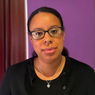 Woman with glasses and necklace against a purple background.