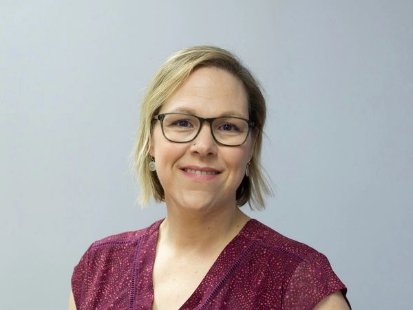 Smiling woman with glasses wearing a maroon top against a plain background.
