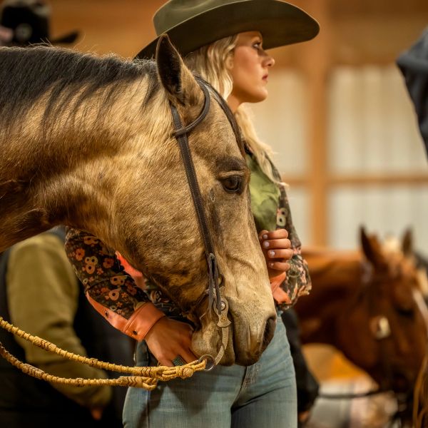A woman in a cowboy hat holding a horse's reins indoors.