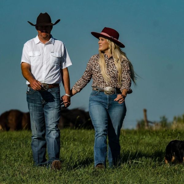 Couple in cowboy hats holding hands and walking in a grassy field.
