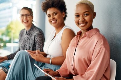 Three diverse women smiling and sitting together.