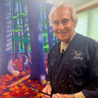 An elderly man painting a vibrant forest scene indoors.