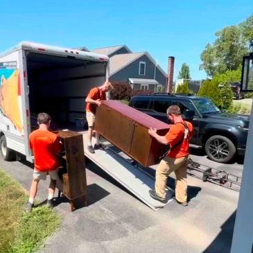 Three movers load furniture from a truck on a hot sunny summer day.
