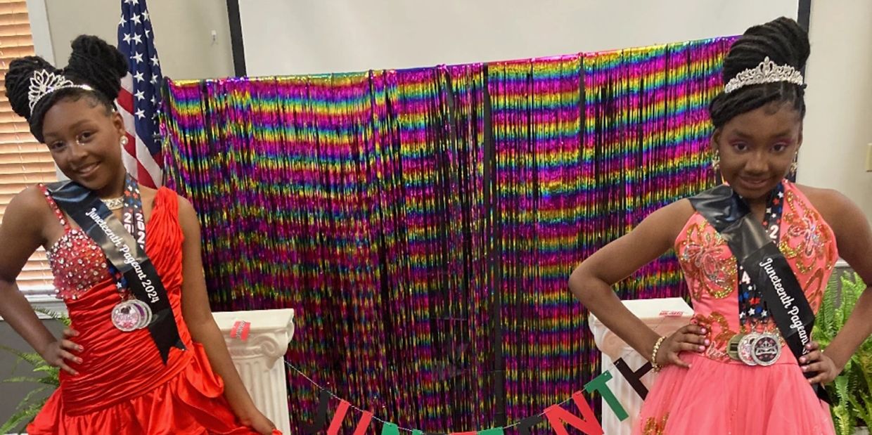 Two girls in pageant dresses with tiaras and sashes posing in front of a colorful backdrop.