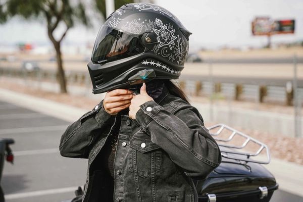 Person wearing a black motorcycle helmet with white designs and a black denim jacket.