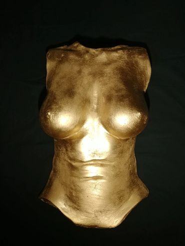 Golden sculpture of a female torso against a dark background.