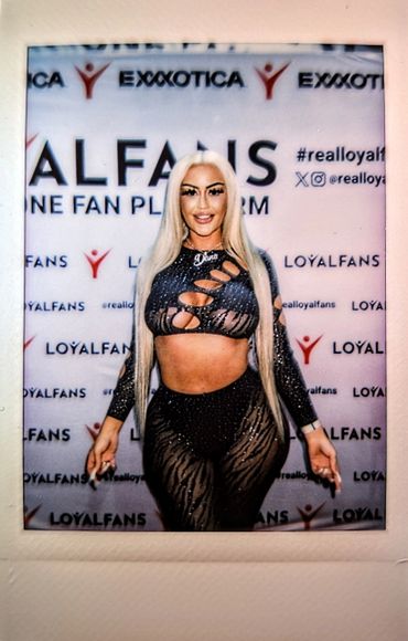 A woman poses confidently in a sheer black outfit at a LoyalFans event.
