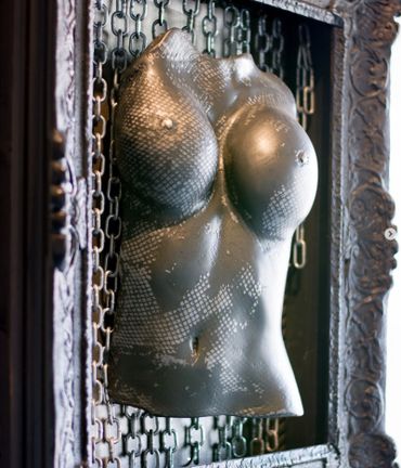 Metallic torso sculpture with snake-like texture in an ornate frame.
