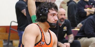 Focused wrestler in orange singlet and headgear during a match.