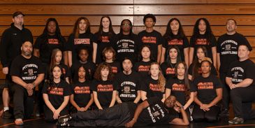 A diverse wrestling team posing for a group photo in a gym.
